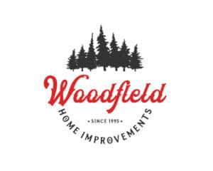 Woodfield Home Improvements logo design featuring a bold red script with evergreen trees—crafted by Inspiring Design Co. to reflect strength, tradition, and craftsmanship.
